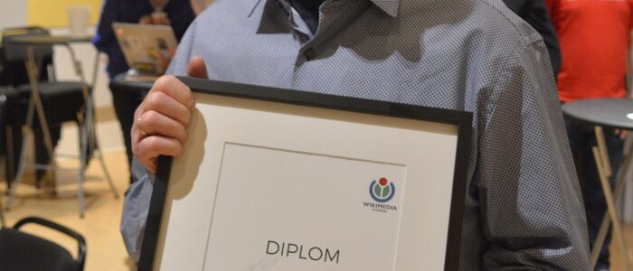 Holger Ellgaard stående med sitt diplom för mottagande av Wikimediapriset framför sig.
